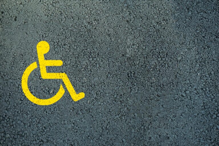 Close-up of a bright yellow disabled symbol on textured asphalt, indicating accessibility.