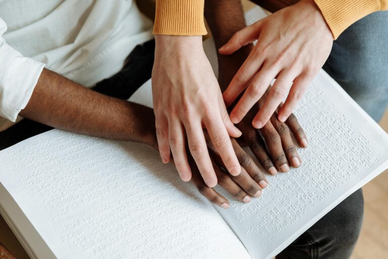 Two people reading a Braille book, representing sensory guidance and inclusion.